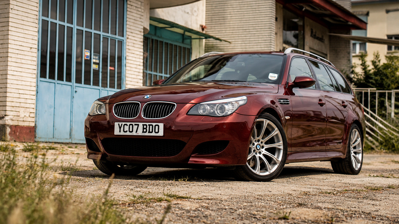 Carro BMW berlina vermelho escuro estacionado numa rua com edifícios ao fundo.